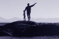 child and woman standing on a rock in the ocean ponting to the next rock